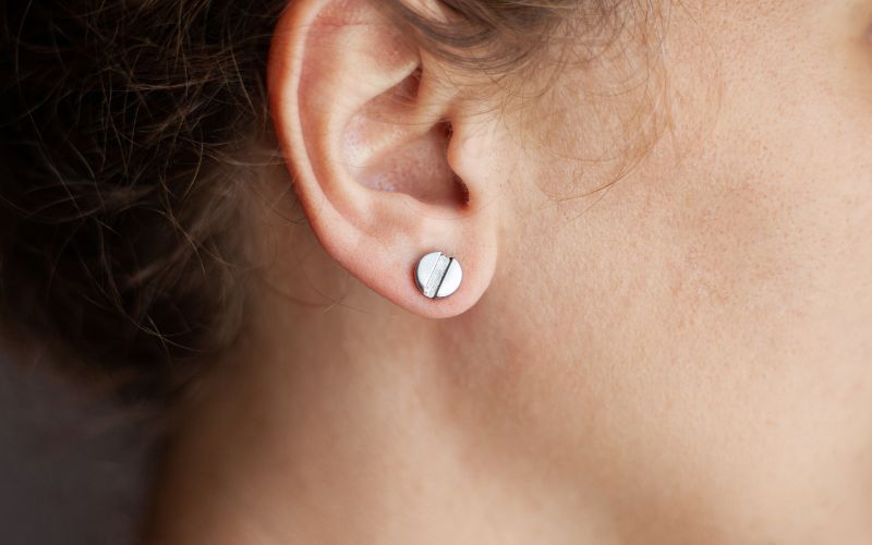 Photo d'une boucle d'oreille médicale sur l'oreille d'une femme de profil, on ne voit que son oreille.