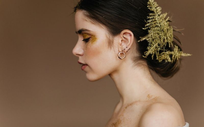 Femme de profil, maquillé et coiffée pour un shooting photo, elle à une belle feuille de fougère dans les cheveux et porte une boucle d'oreille en acier inoxydable.