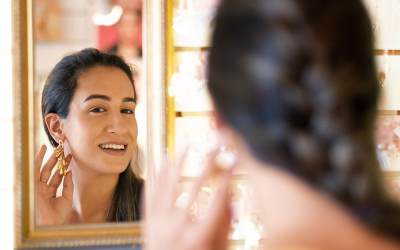Jeune femme devant un miroir qui admire une boucle qu'elle porte à l'oreille.