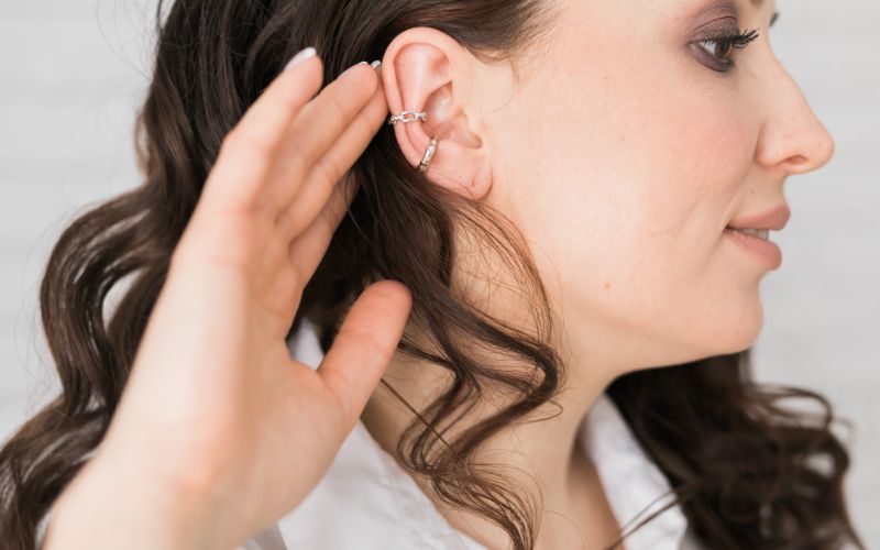 Femme de profil qui porte deux ear cuff sur une oreille, elle approche sa main de son oreille.
