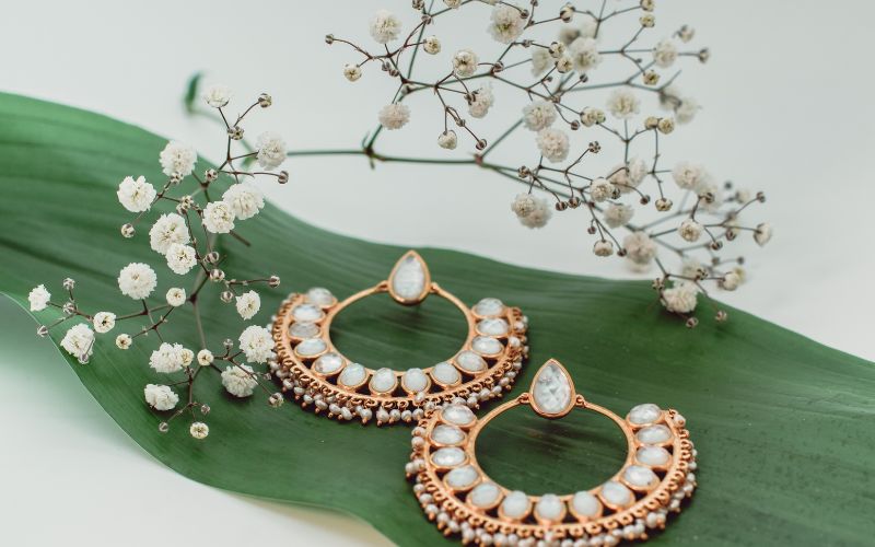 Paire de boucle d'oreille présenté sur une large feuille de plante verte avec un petite branche de fleurs blanches