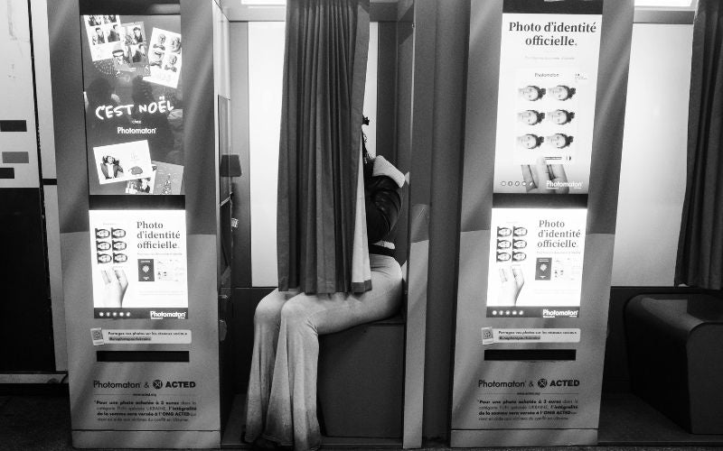 Personne assise derrière le rideau d'un photomaton pour faire des photos d'identités