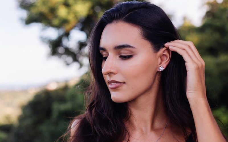 Femme avec les cheveux long et détachés qui se glisse un mèche derrière l'oreille ou se trouve une belle boucle en diamant.