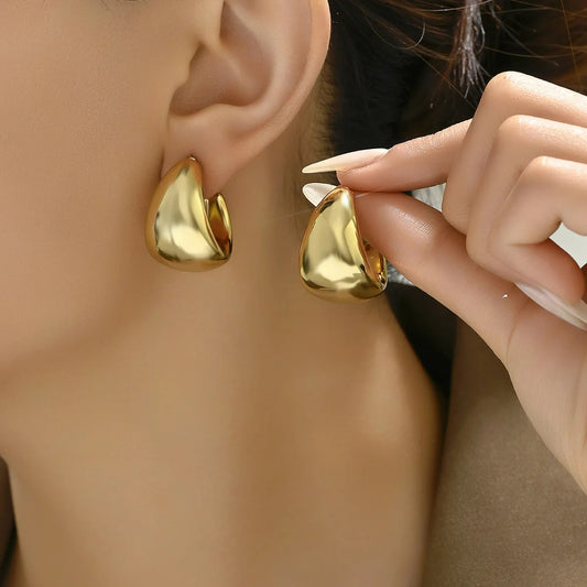 Boucle D'oreille Créole Large Moderne portée par une femme, elle tient l'autre boucle dans ses doigts et la présente à côté de son oreille.