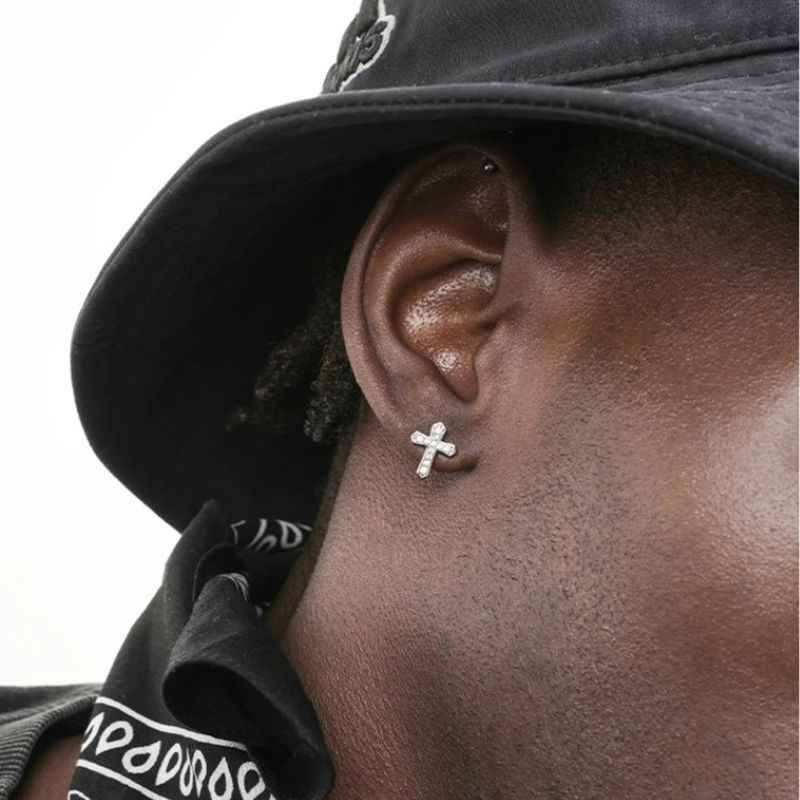 Boucle D'oreille Croix Homme Argentée à Strass portée par un homme de profil avec un bob, on ne voit que sa joue et son oreille