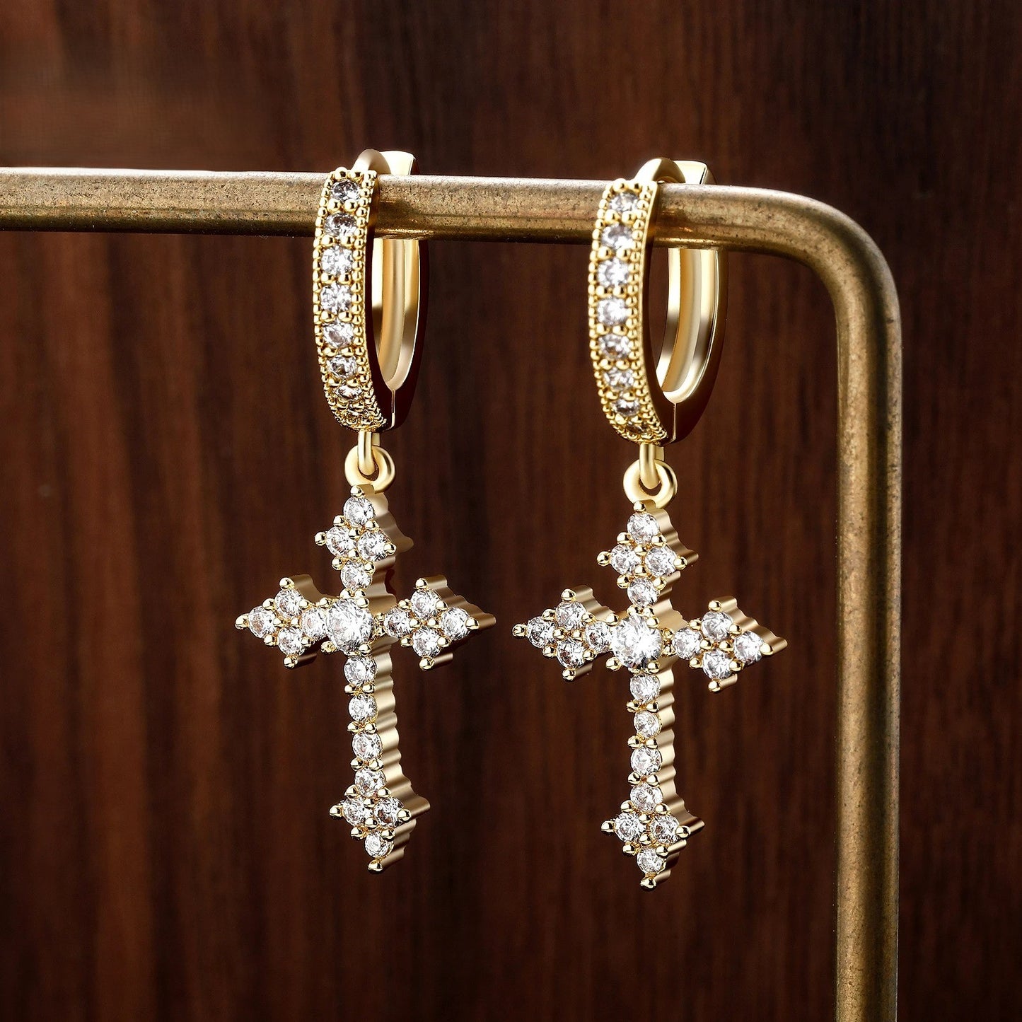 Boucle d'Oreille Croix Homme Dorée Pendante sur présentoir tige doré, arrière plan bois foncé