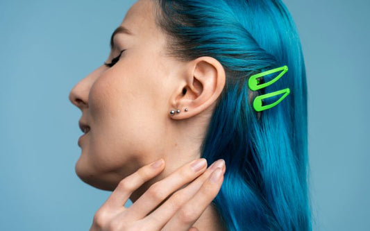 Femme avec les cheveux bleu, de profil qui porte 3 boucles d'oreille puce à une oreille