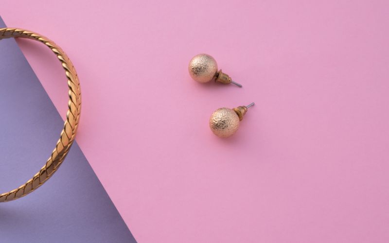 Paire de boucle d'oreille boucle dorée martelée, avec un fermoir poussoir en forme de cône, posé sur un papier rose bonbon Image