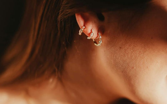 Oreille de femme avec bas du coup et ses cheveux longs, elle porte 3 anneaux boucle d'oreille 3 trous. 