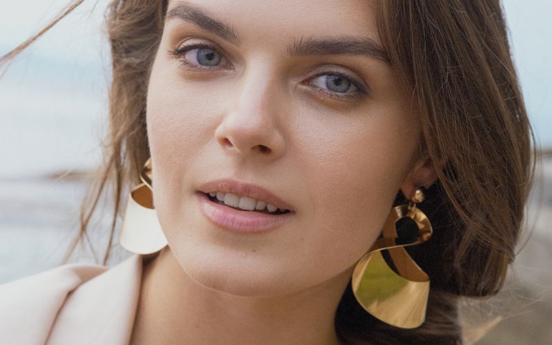 Femme portant des grande boucle d'oreilles pendantes dorées en acier inoxydable. On voit la mer derrière elle. Image
