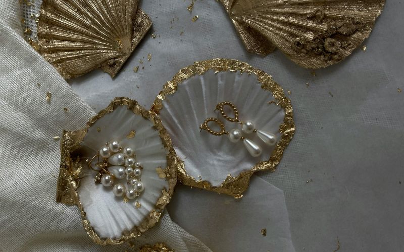 Boucle d'oreille en perle de coquillage, présentés dans des coquille saint jaque décoré avec un liseré doré sur un linge en lin blanc.