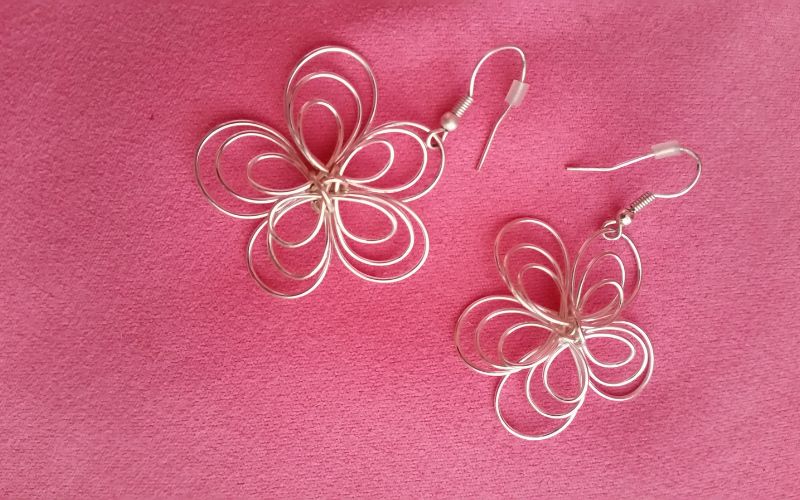 Boucle d'oreille en forme de fleur pendante faite en fil en acier inoxydable sur un fond rose bonbon