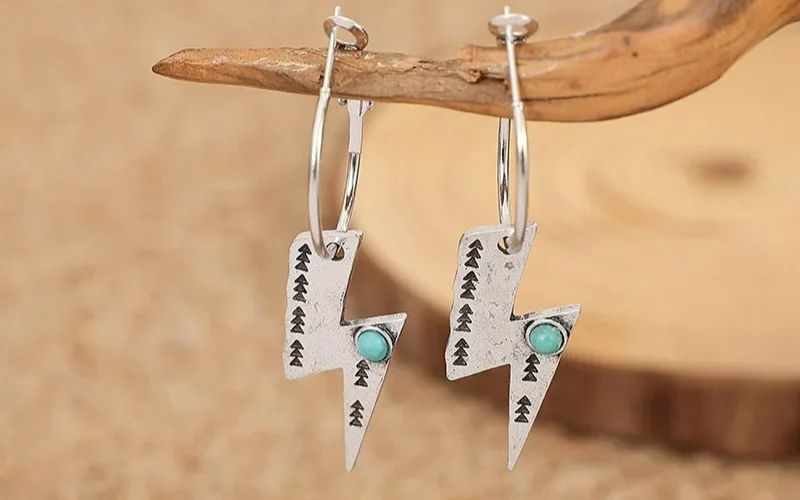 Paire de boucle d'oreilles éclair pendante argenté et petite pierre bleu suspendu sur une petite branche de bois.