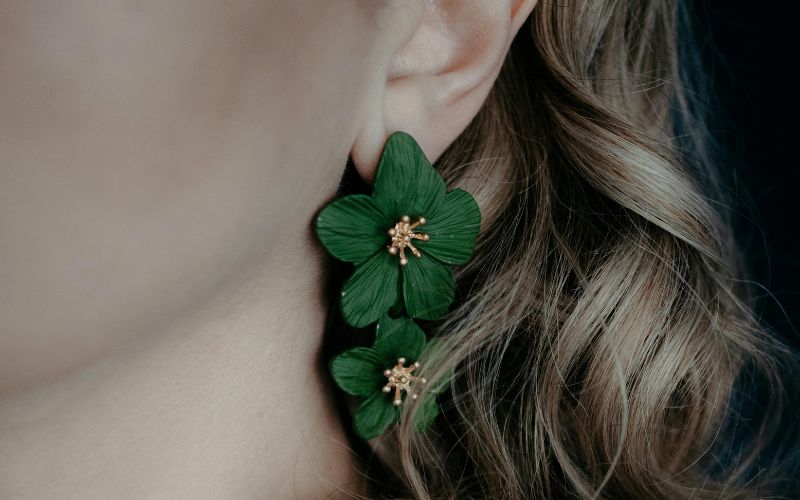 Femme portant une boucle d'oreille avec 2 fleurs vertes pendantes. on ne voit que son oreille ses cheveux derrière la boucle d'oreille.