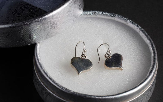 Boîte ronde grise métallique, avec un coussin blanc et une paire de boucle d'oreille cœur argentée pendante