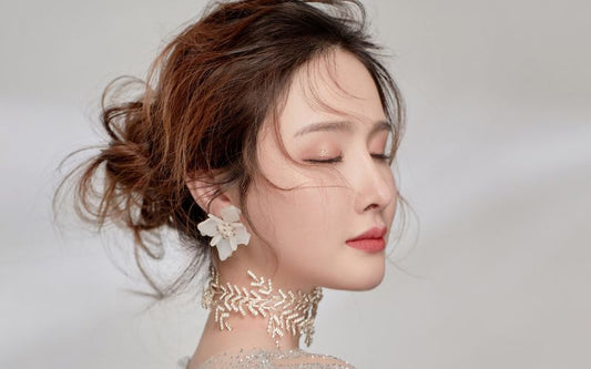 Femme cheveux attachés effet coiffé décoiffé, portant un collier de feuilles fines et délicates et des boucle d'oreille à clip en forme de fleur réaliste.