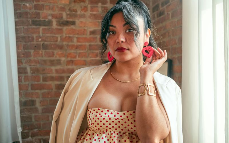 femme vêtue d'une robe a pois, d'un gilet beige et de bijoux, dont une paire de boucle d'oreille cœur rouge pendante Image