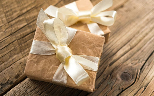 Petite boite cadeau marron clair avec un ruban jaune très clair satiné sur une table en bois.