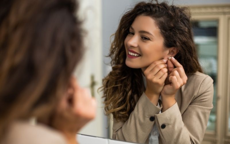 Femme devant son miroir dans sa salle de bain, elle enlève une boucle d'oreille. Image