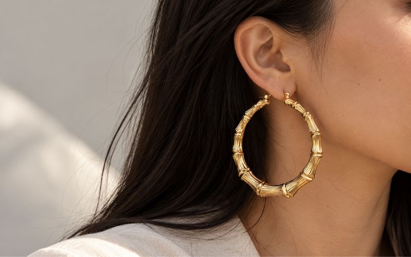 Femme de profil, cheveux noir longs, détachés, on ne voit pas sont visage, elle porte une boucle d'oreille créole grande dorée effet bambou 