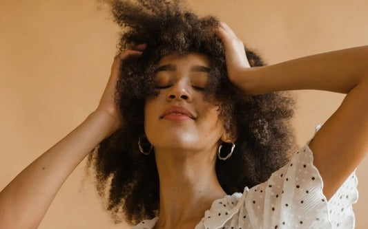 Femme qui pose pour la photo avec un fond orangé pâle, qui porte une paire de créole classique argenté.