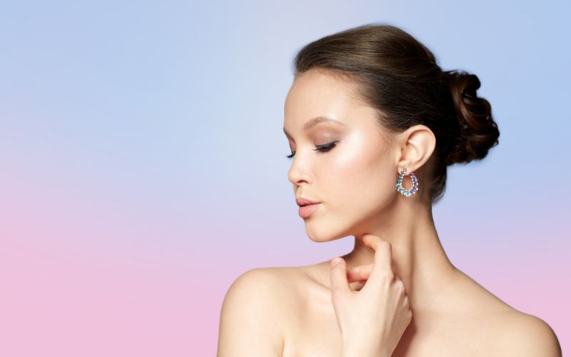 Femme de profil, qui pose sur un fond dégradé du rose au bleu, elle porte de magnifique créole fleuris strass effet diamant Image