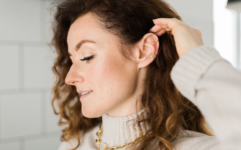 Femme de profil qui relève ses cheveux pour montrer les deux ear cuff qu'elle porte sur une oreille. Image