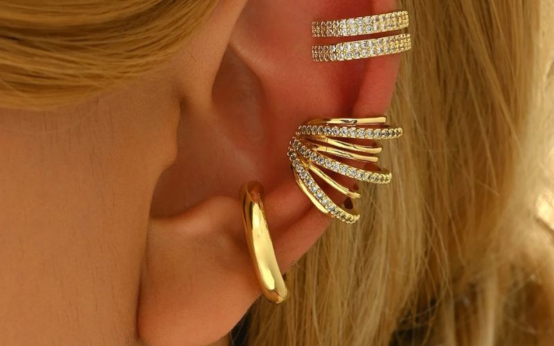 Plusieurs ear cuff doré et brillant sur l'oreille d'une femme blonde. Image