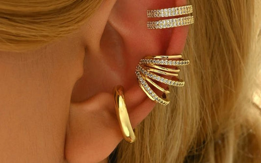 Plusieurs ear cuff doré et brillant sur l'oreille d'une femme blonde.