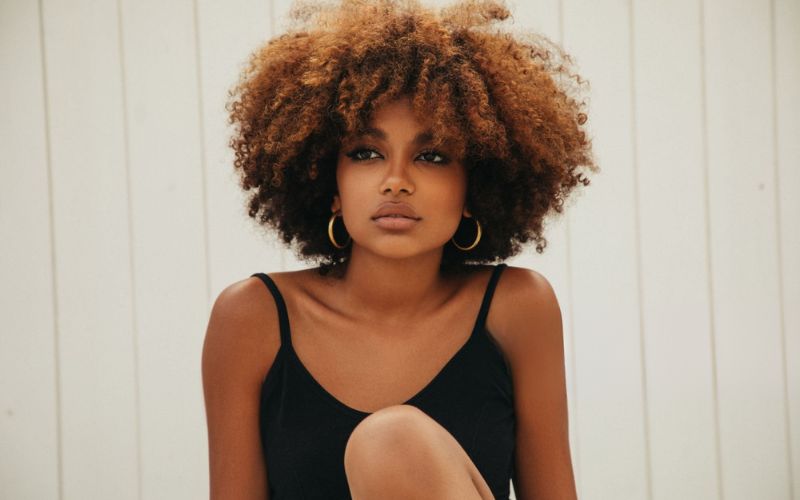 Femme devant bardage en bois blanc, qui porte une paire de créole doré assez grande et une robe noire avec des bretelles Image