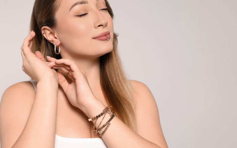 Femme les yeux fermés, avec des boucles d'oreilles et un anneau comme piercing à la lèvre inférieur, ses deux mains se dirige vers ses boucles d'oreilles Image