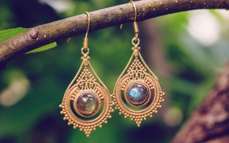 Belles boucle d'oreilles pendantes en or avec une pierre précieuse au centre de chaque boucle, suspendues sur une branche d'arbre Image
