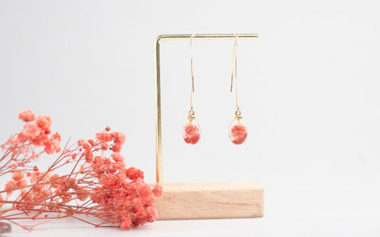 Paire de boucle d'oreille pendue sur un support bois et métal minimaliste et élégant. avec des fleurs séchés roses à côté