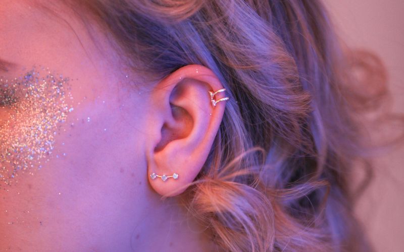 Femme coiffée et maquillée pour une fête, on voit son profil visage et cheveux, elle porte des boucles d'oreille cartilage anneau en haut de l'oreille. Image