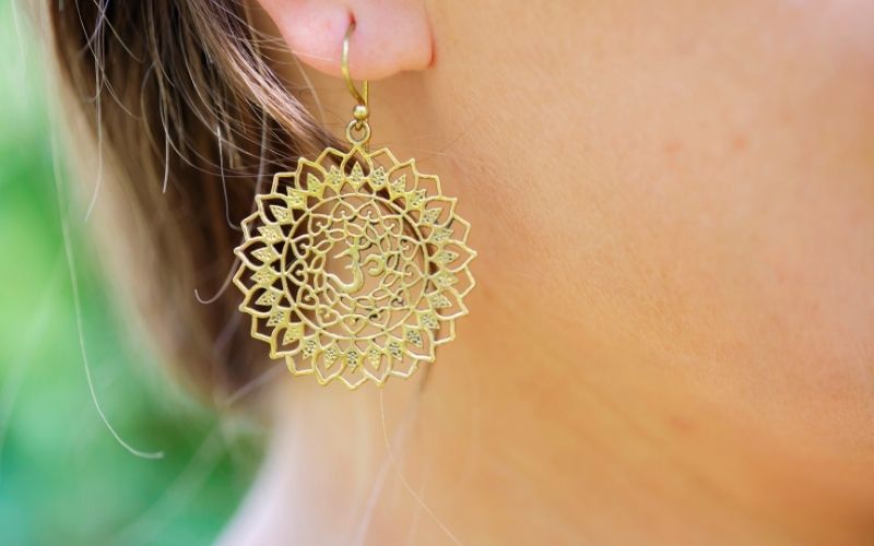 Femme qui porte un boucle assez grande pendante dorée, en fleur de vie et signe OM.