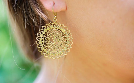 Femme qui porte un boucle assez grande pendante dorée, en fleur de vie et signe OM.