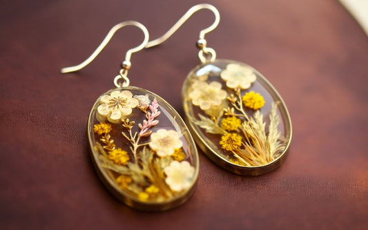 Paire de boucles d'oreilles ovales plates avec de véritable fleurs emprisonnées dans de la résine, posées sur un plateau marron foncé marbré