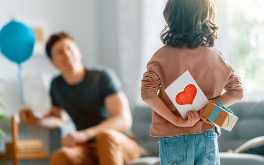 Un enfant face à son papa qui cache dans son dos une carte et un cadeau pour la fête des pères.