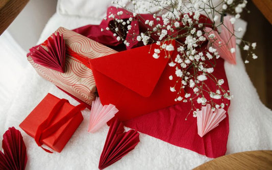 table blanche sur laquelle est posé deux cadeaux et une décoration Saint Valentin, avec des coeurs rouge, roses, des petites fleurs blanche, une enveloppe rouge.