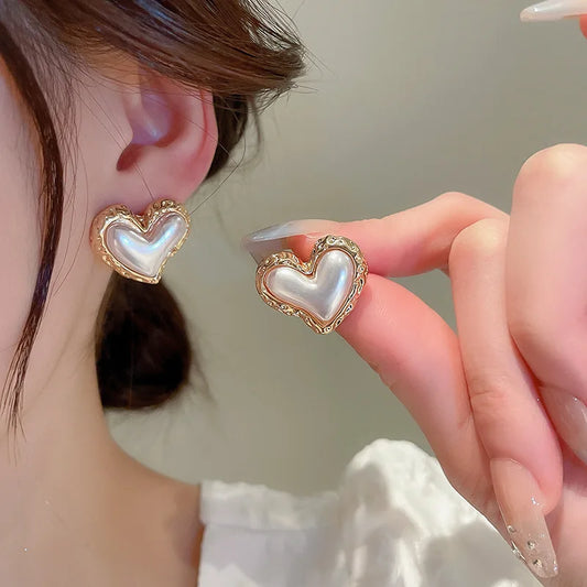 Boucle d'Oreille Acier Inoxydable Cœur Nacré, portée par une femme, elle tient l'autre boucle dans ses doigts à côté de celle à son oreille.