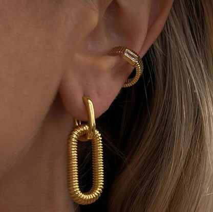 Boucle d'Oreille Acier Inoxydable Dorée, portée par une mannequin avec une autre boucle d'oreille dorée, on voit son oreille et les boucles en gros plan.