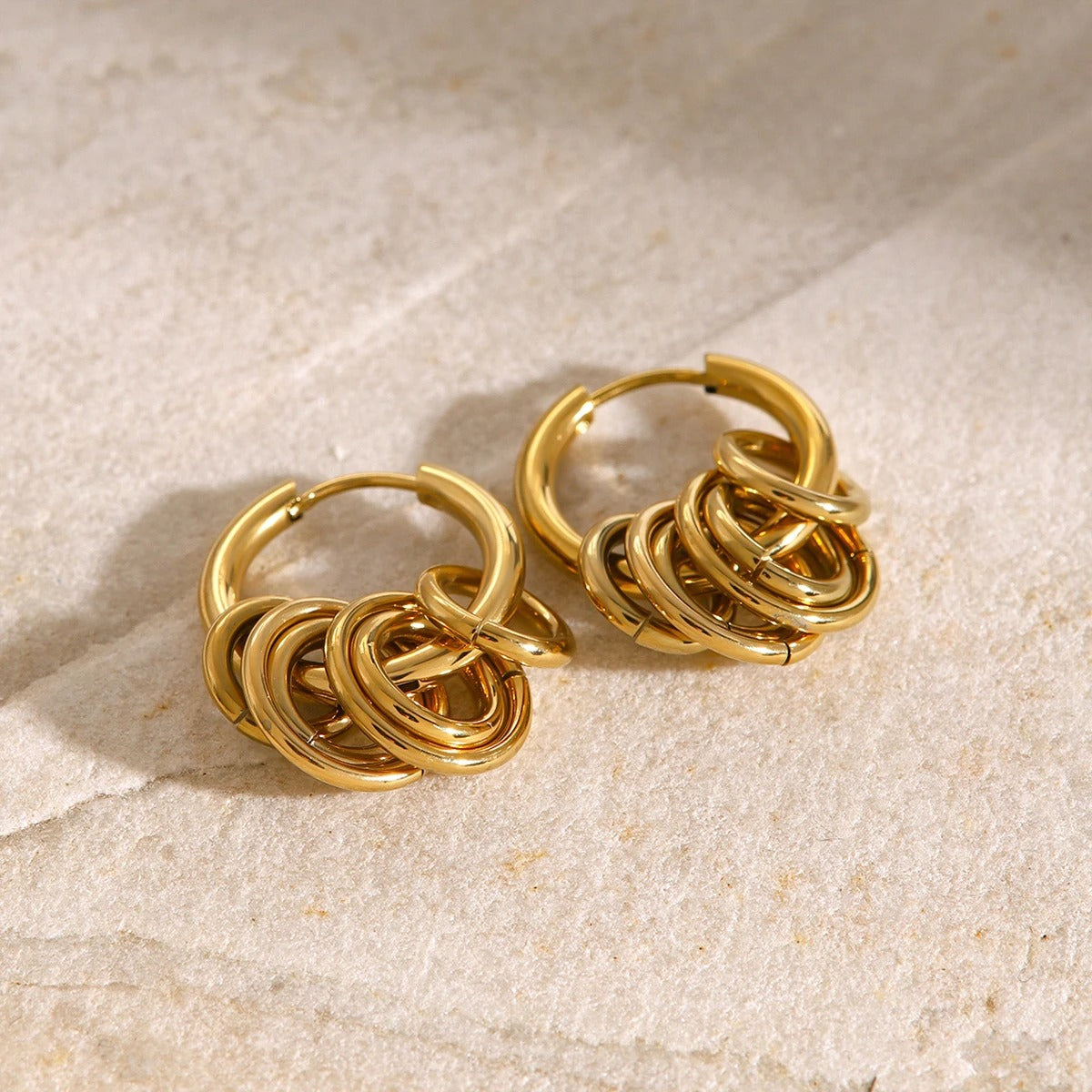Boucle D'oreille Anneau Femme Multi-Cercles Dorés, présentées en paire posées sur une pierre beige clair Image
