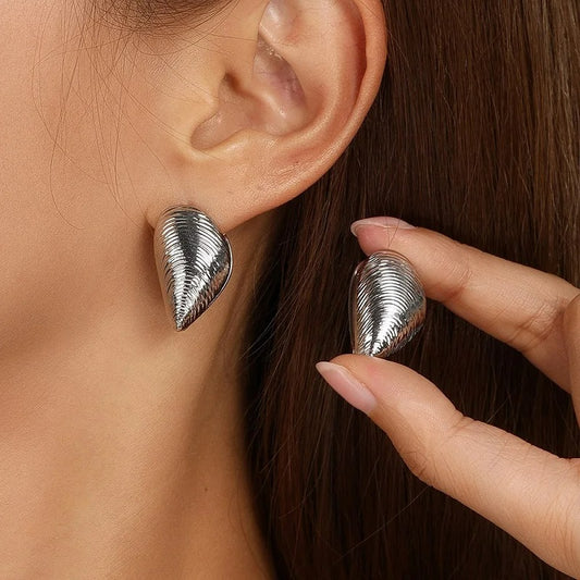 Boucle D'oreille Coquillage Argenté, portée par une femme, elle présente l'autre boucle entre ses doigts à côté de son oreille