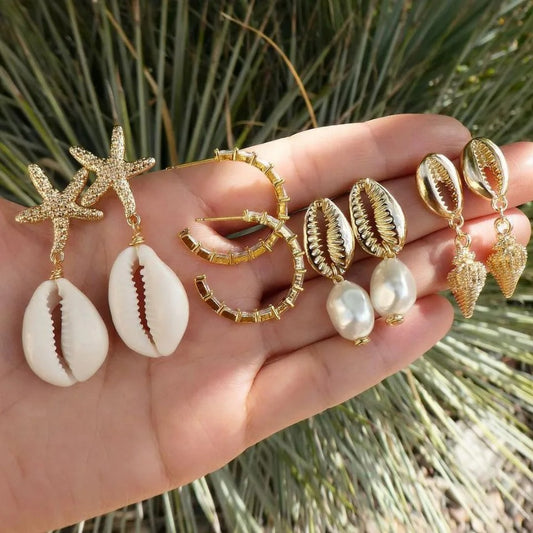 Boucle D'oreille Coquillage Lot De 4 présentées sur la mains d'une femme avec des plantes vertes en fond