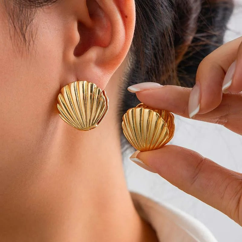 Boucle D'oreille Coquillage Vintage Doré, portée par une femme de profil, elle présente l'autre boucle d'oreille entre ses doigt à côté