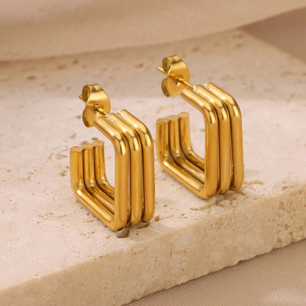 Boucle D'oreille Créole Carrée en acier inoxydable, présenté en paire sur une plaque de pierre beige.