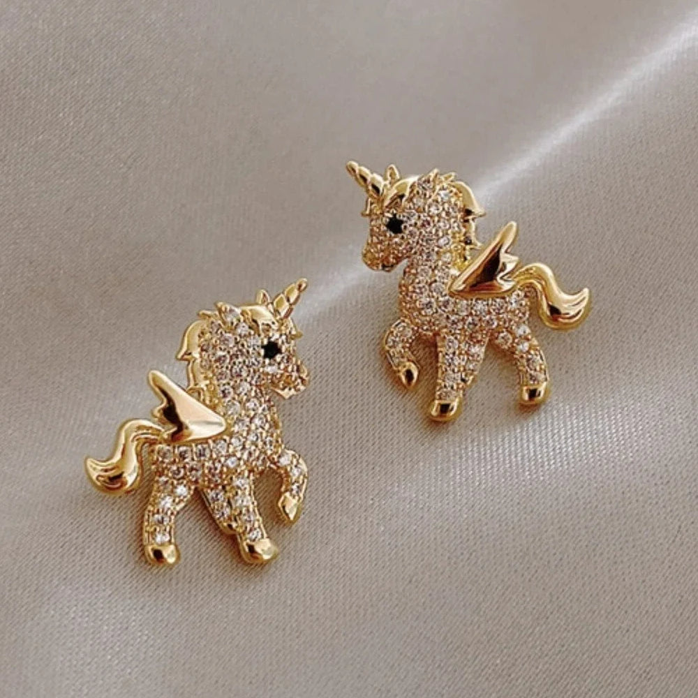 Boucle d'Oreille Enfant Sublime Licorne doré avec des strass présenté sur tissu satin beige.