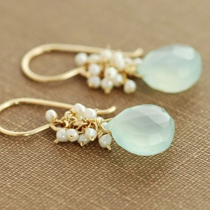 Boucle D'oreille fantaisie effet goutte présenté sur un tissu doré effet toile de jute.