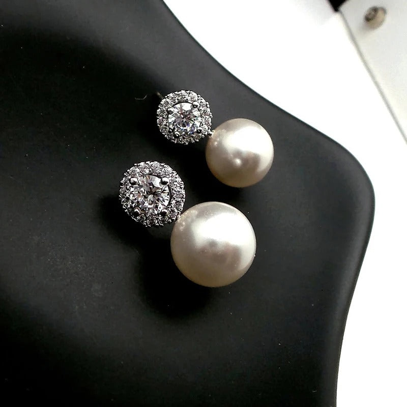 Boucle d'Oreille Femme Perle Blanche avec Petit Diamant posé sur un tissu noir  Image