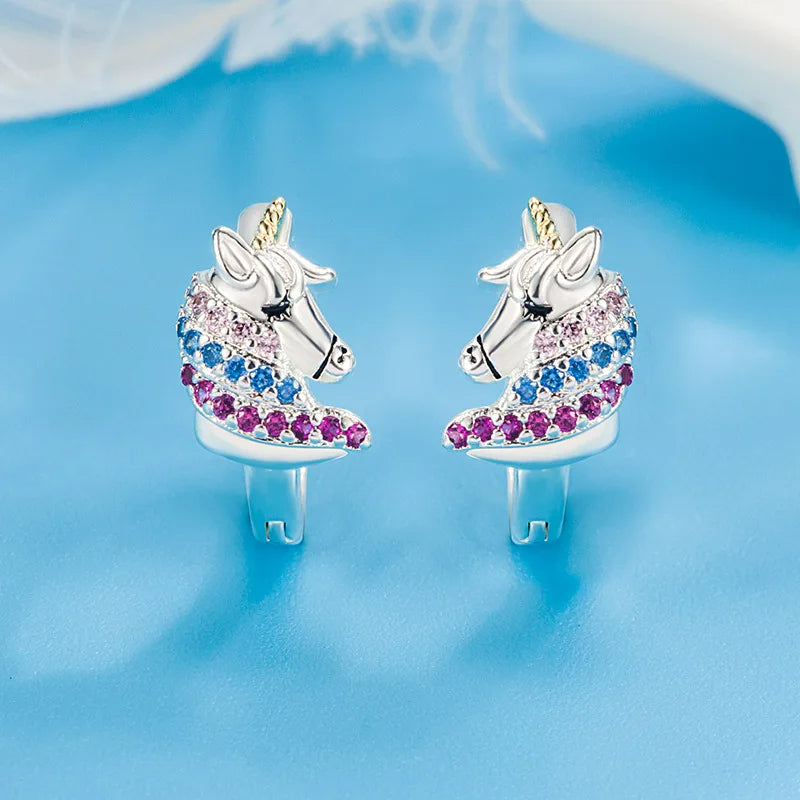 Boucle D'oreille Licorne Féerique Argentée, présenté sur un fond bleu clair.